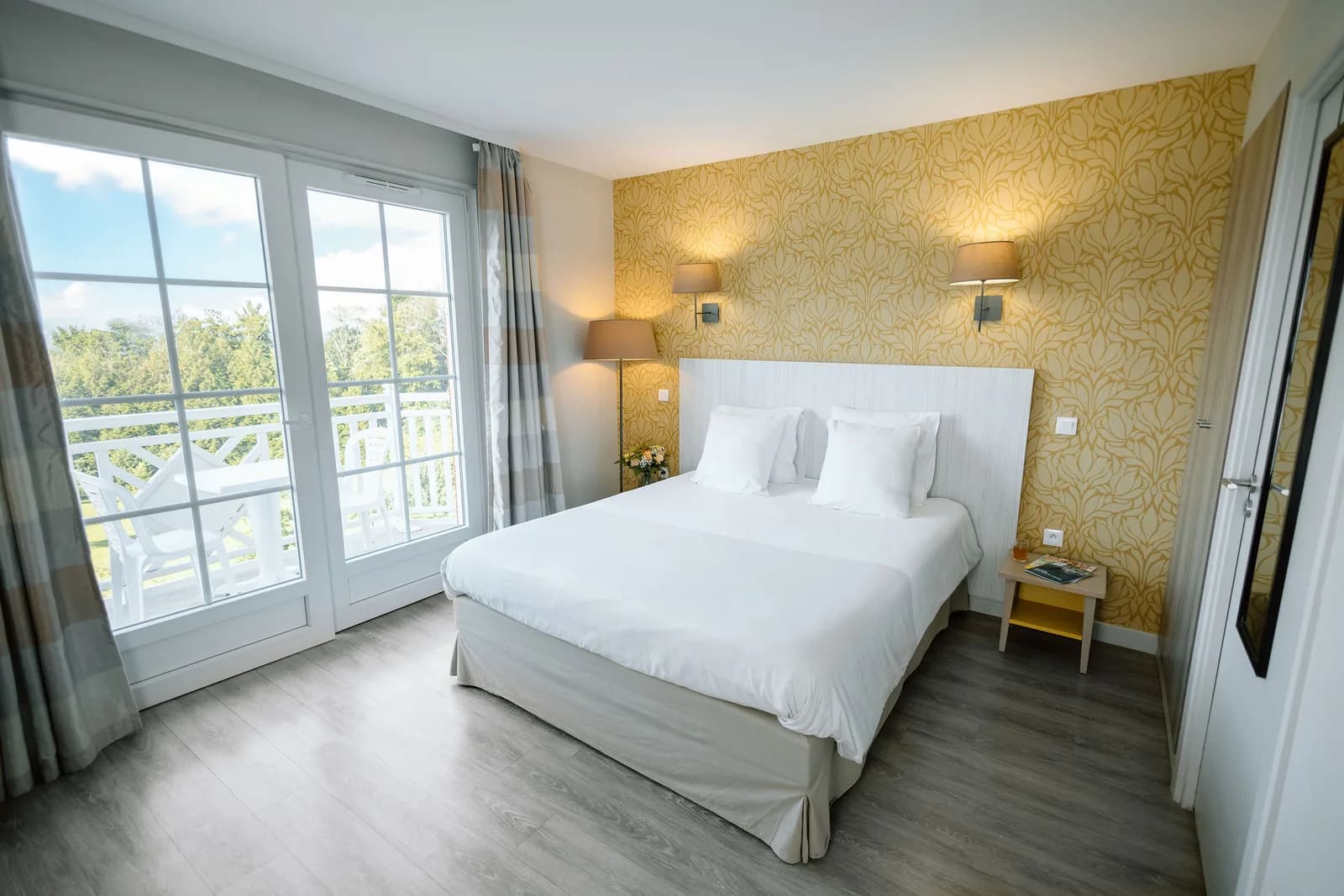 Chambre avec lit double, papier peint doré et porte-fenêtre donnant sur un balcon