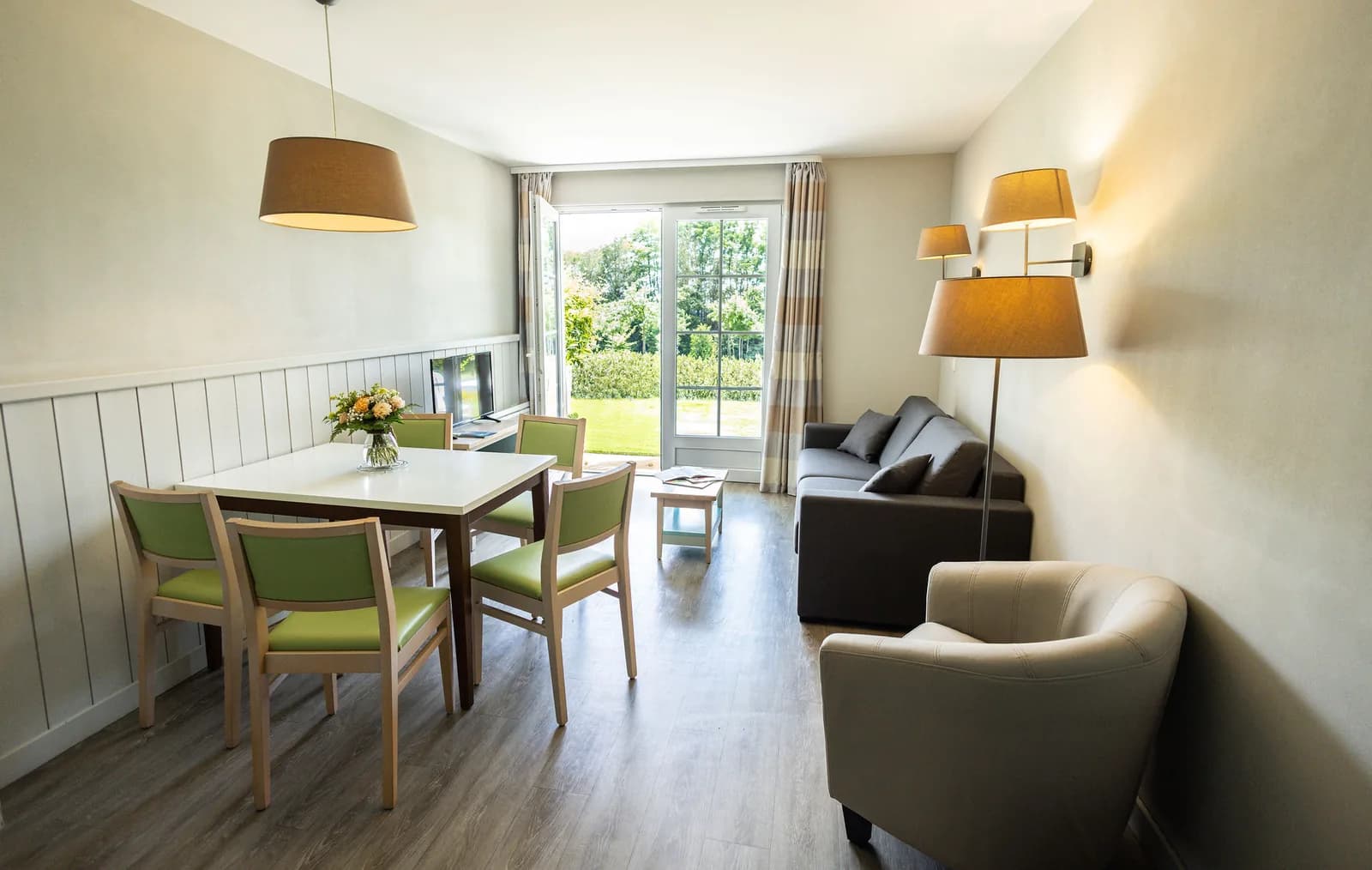 Séjour d'un appartement : table à manger, canapé et baie vitrée ouvrant sur le jardin