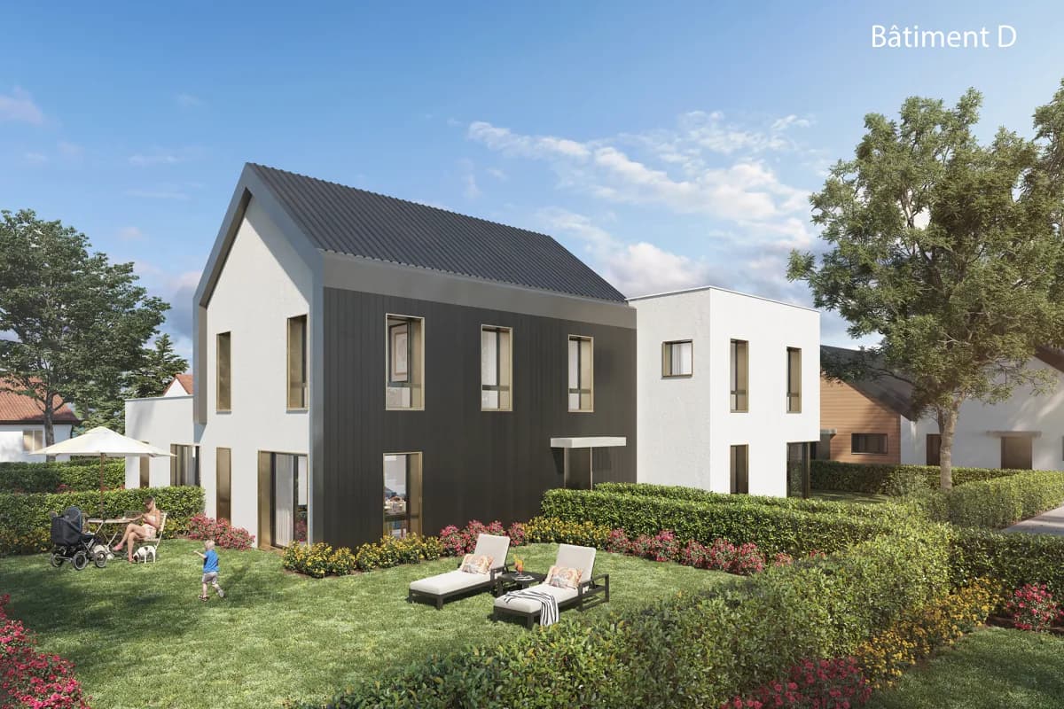 Bâtiment D côté jardin : pignon blanc et façade en bardage sombre, toiture à deux pentes en zinc, pelouse, haies et transats