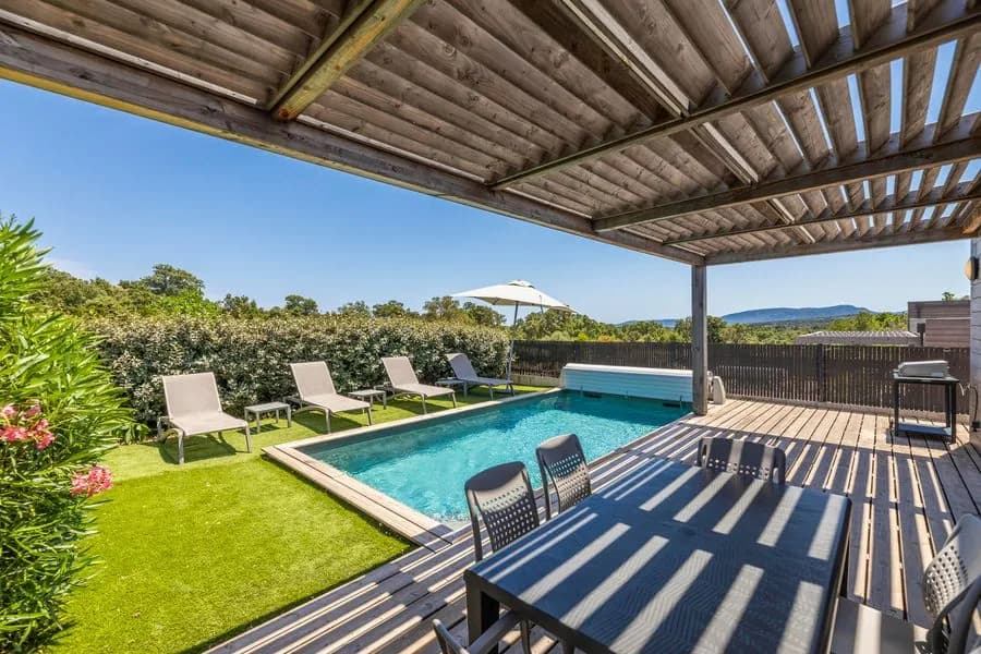 Terrasse privative d’une villa sous pergola en bois : piscine, transats, table de repas et vue dégagée sur les collines