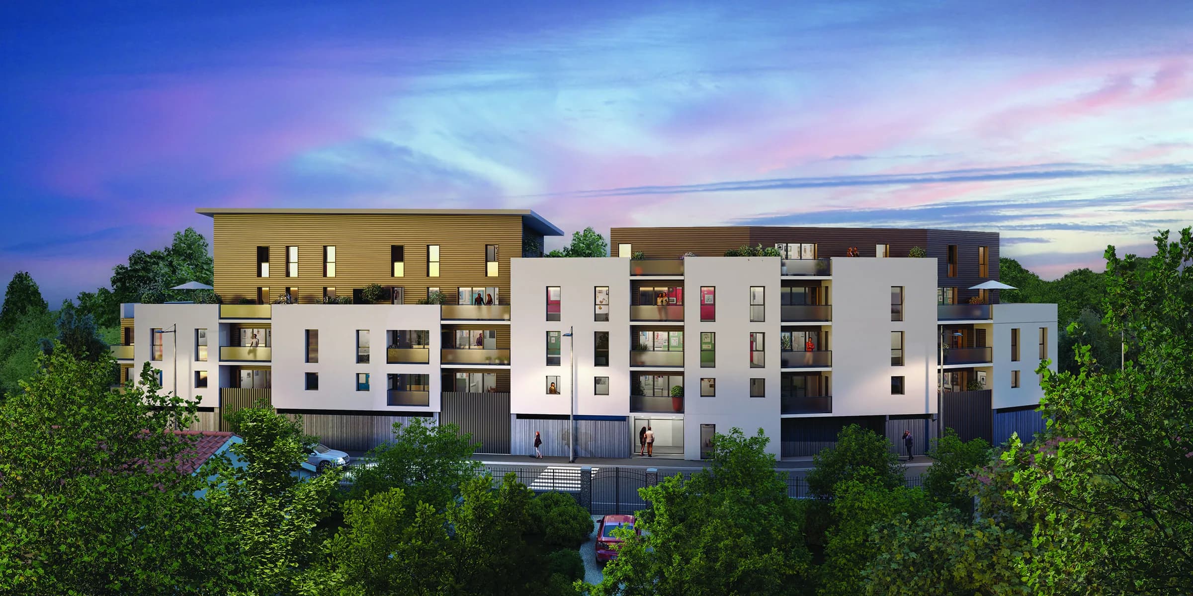 La résidence vue de la rue au crépuscule : volumes blancs et bardage bois doré, balcons en encorbellement, appartements éclairés, ceinturée d’arbres