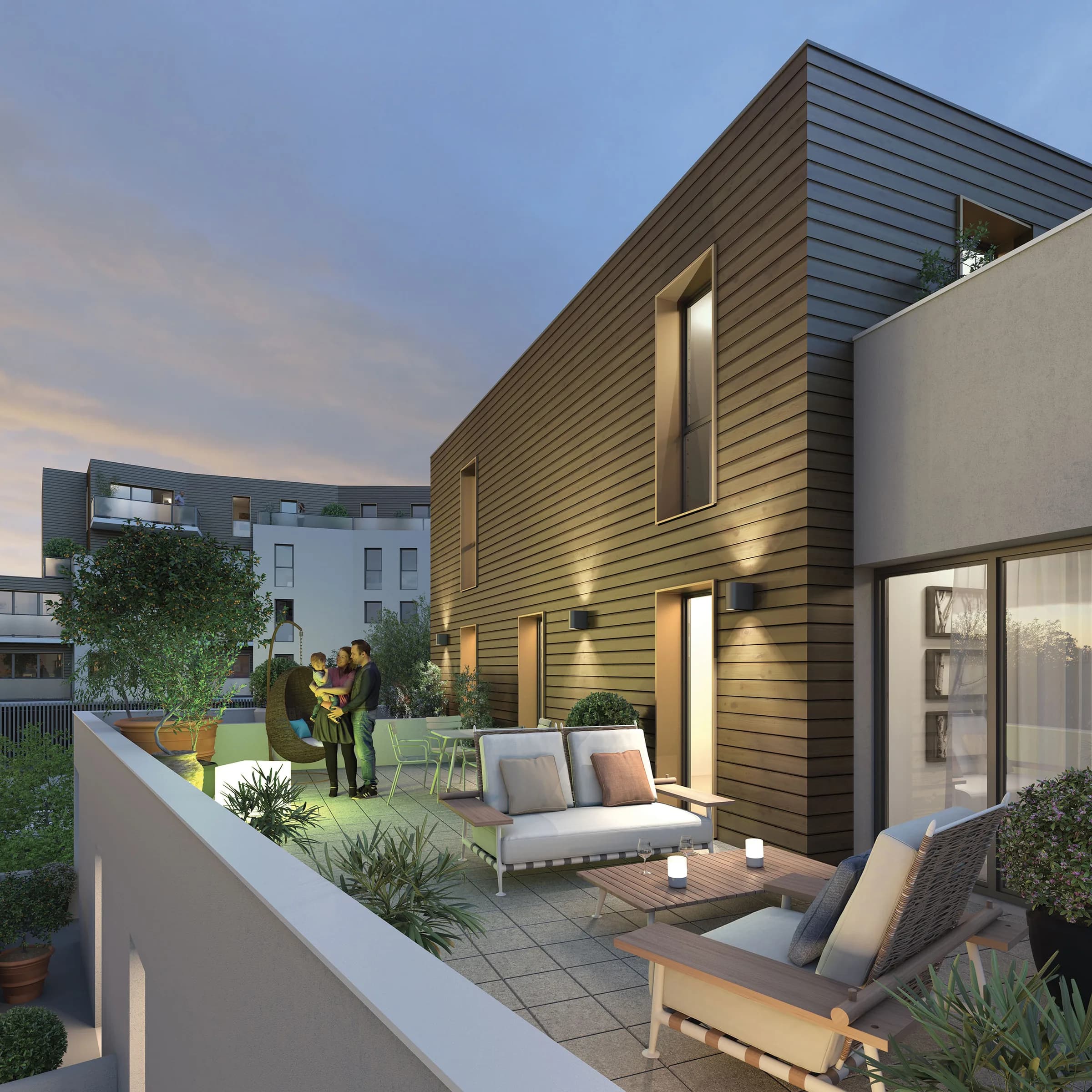 Terrasse d’un appartement au crépuscule : banquettes et bain de soleil en rotin, citronnier en pot et fauteuil suspendu, contre un volume bardé de bois clair éclairé par des appliques ; une famille au fond