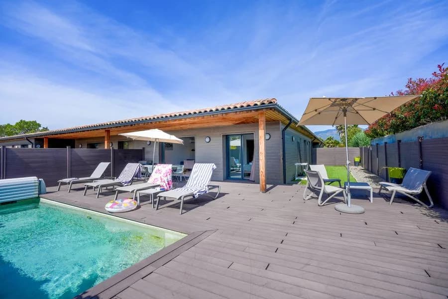 Terrasse d’une villa et sa piscine privative : bardage bois, larges baies, transats, parasols et haie de séparation